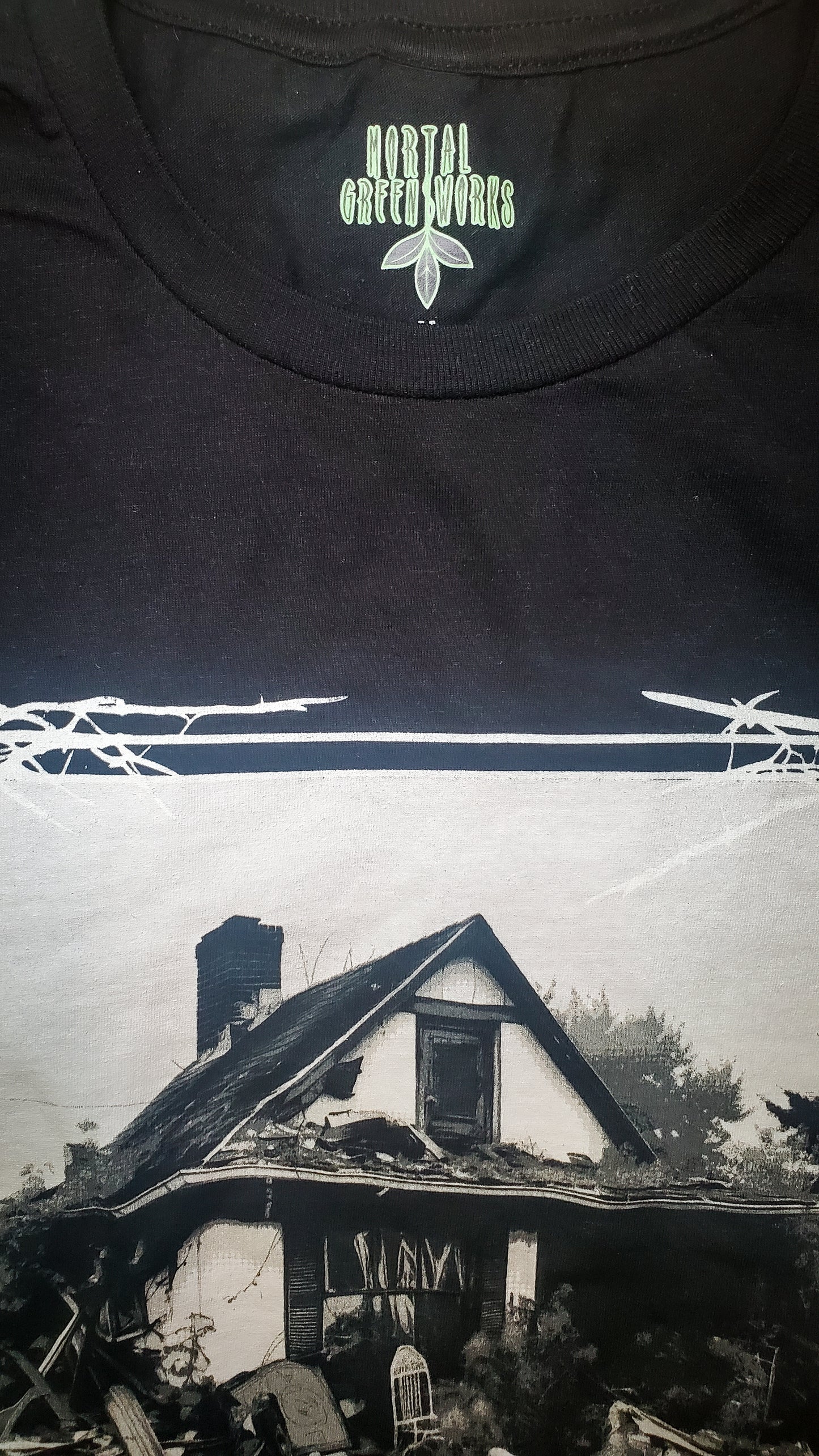 Detail of Mortal Greenworks logo on a black T-shirt with a haunting cottage garden graphic, merging homesteading with dark humor