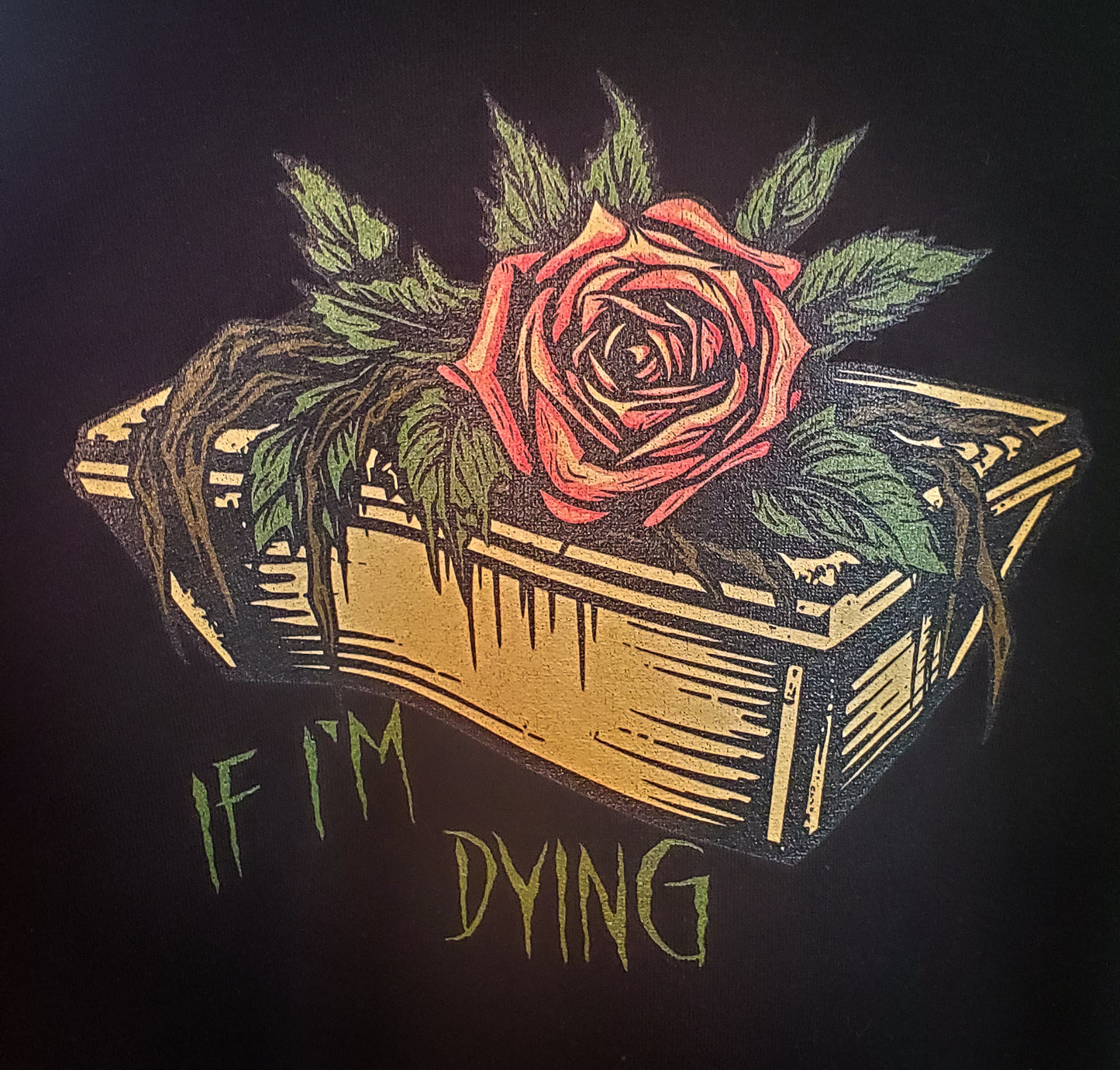 Close-up of a black hoodie's gothic print featuring a vibrant rose growing from a coffin, with the darkly humorous phrase 'IF I'M DYING.'