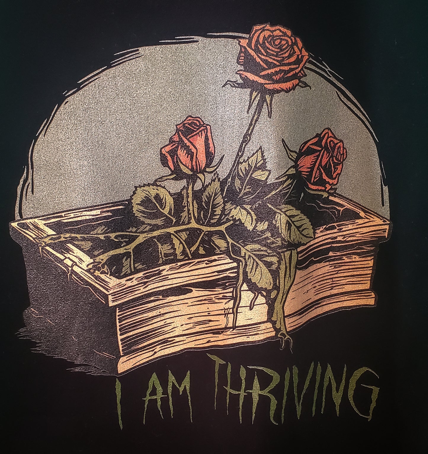 Detailed graphic on the back of a black hoodie depicting roses thriving in a coffin, with the statement 'I AM THRIVING,' set in a Cottagecore Horror style.