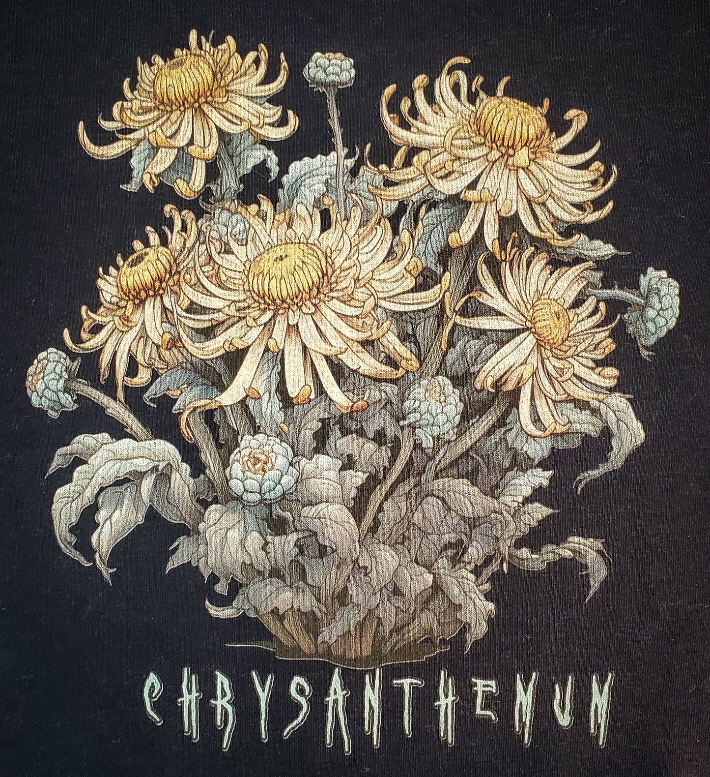 Close-up of black sweatshirt with intricate chrysanthemum illustration in gold tones, emphasizing the Cottagecore Horror theme.