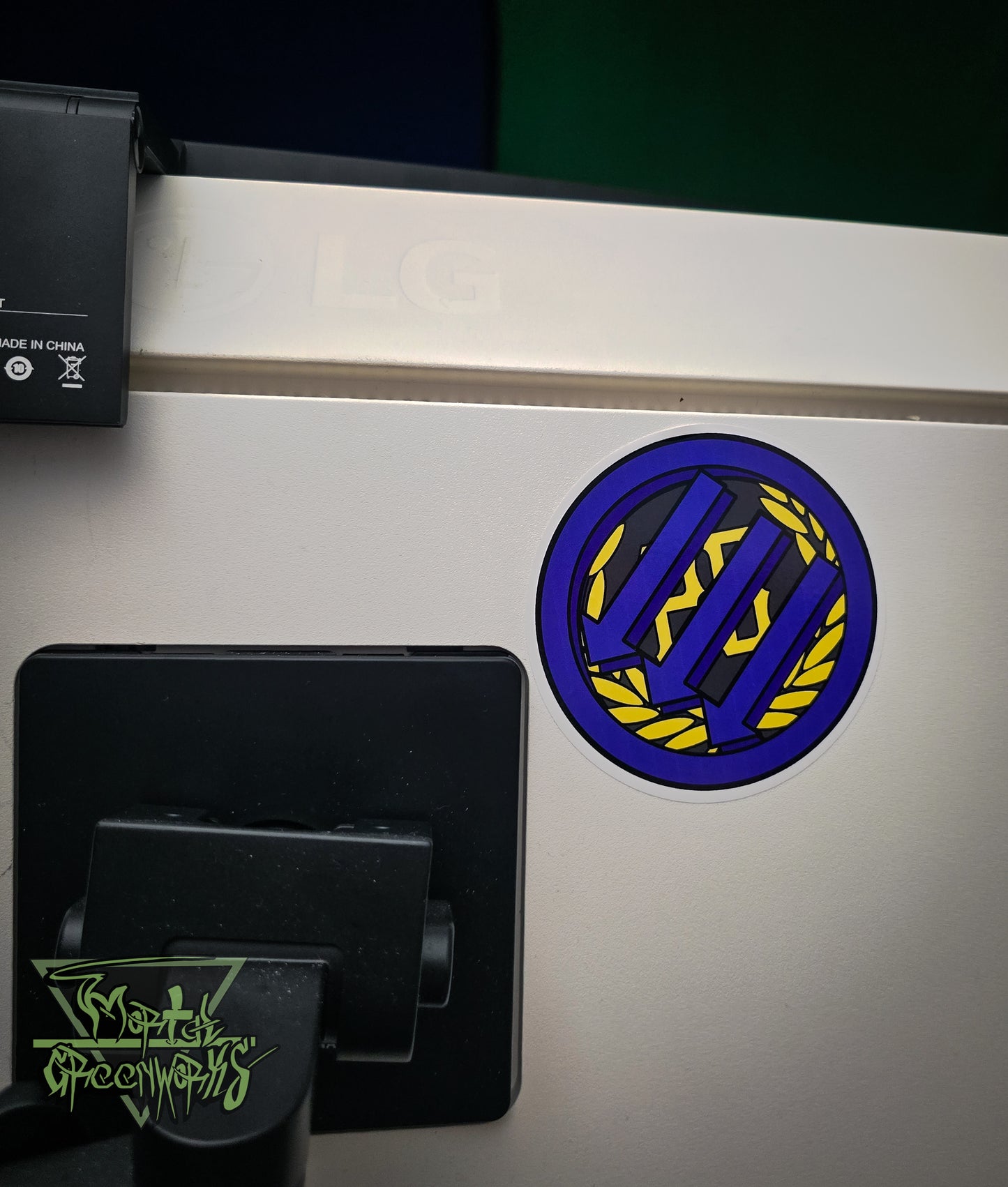 Close up of a sticker placed on the back of a PC. The purple Iron front logo of three down arrows covers up the golden proud boy logo behind it.