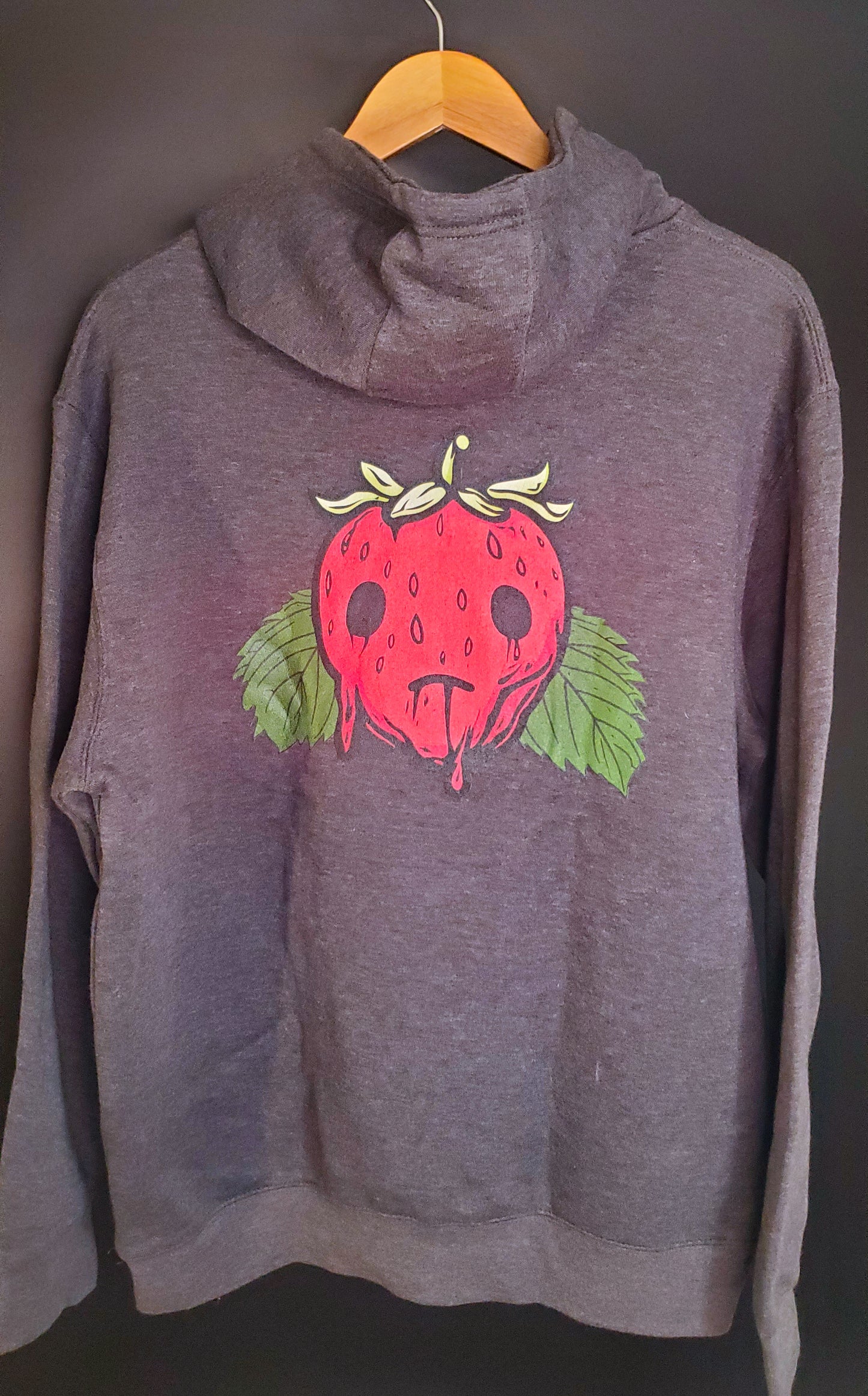 The back of a gray hoodie with a red strawberry graphic sits on a hanger against a dark background