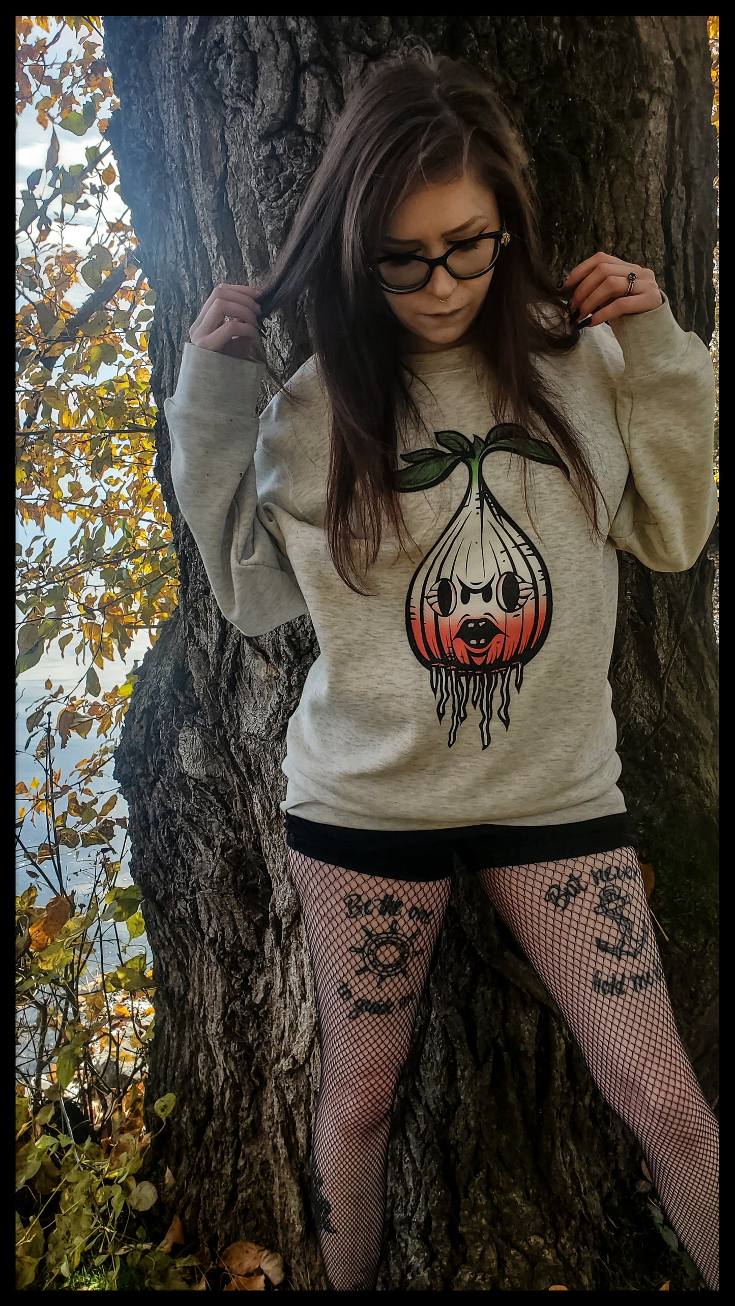 Girl in an oatmeal heather sweatshirt adorned with a graphic of a radish. The radish is intricately designed with roots extending downward, creating a natural, earthy aesthetic. The radish sports a whimsical face, infusing the design with character.
