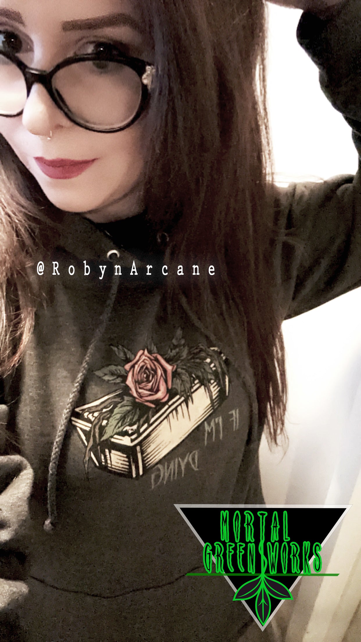 Individual posing in a black hoodie with a rose and coffin design and 'IF I'M DYING' text, under the Mortal Greenworks logo, tagged @RobynArcane.
