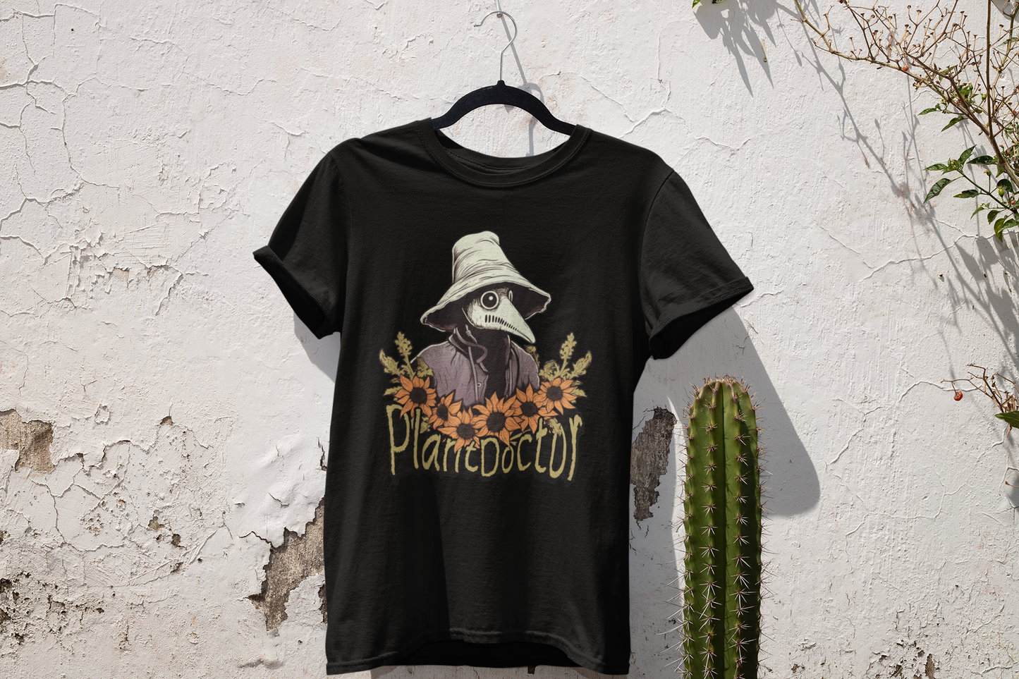 Black t-shirt featuring a 'Plant Doctor' graphic on display against a textured white wall, accented by desert plants, reflecting a modern botanical theme.