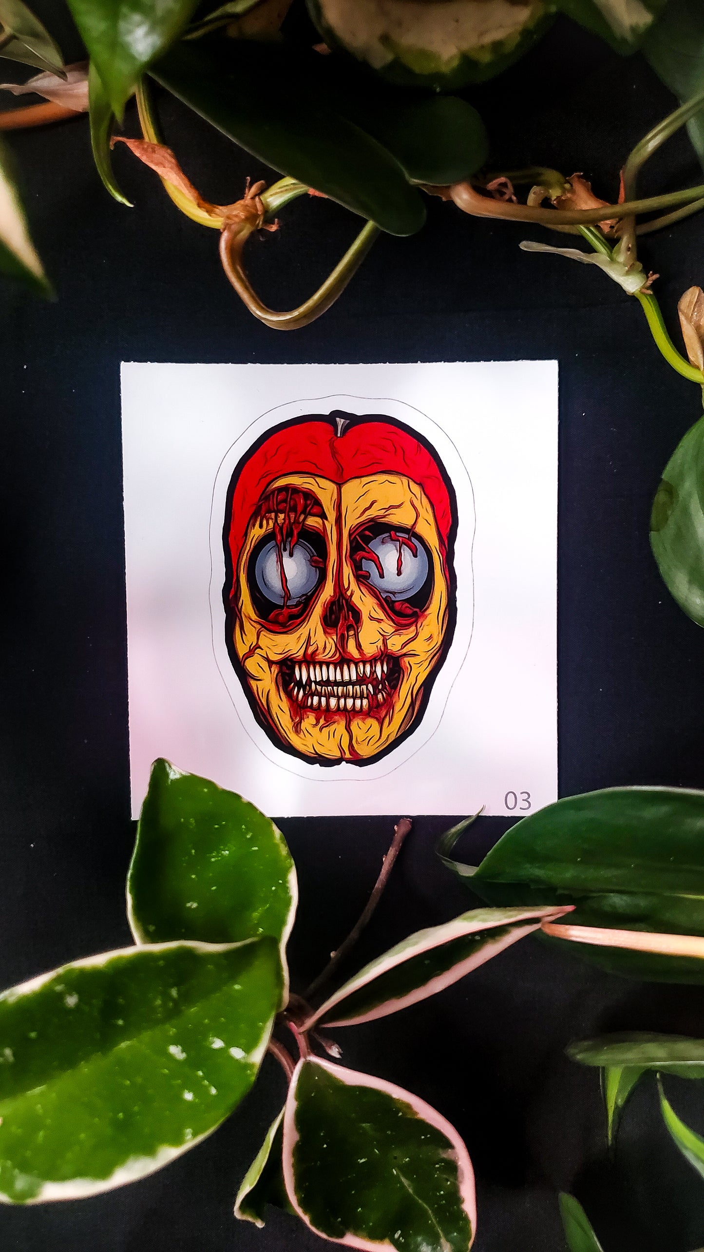 A sticker of a cut open passion fruit resembling a skull on a dark background, framed by green leaves.