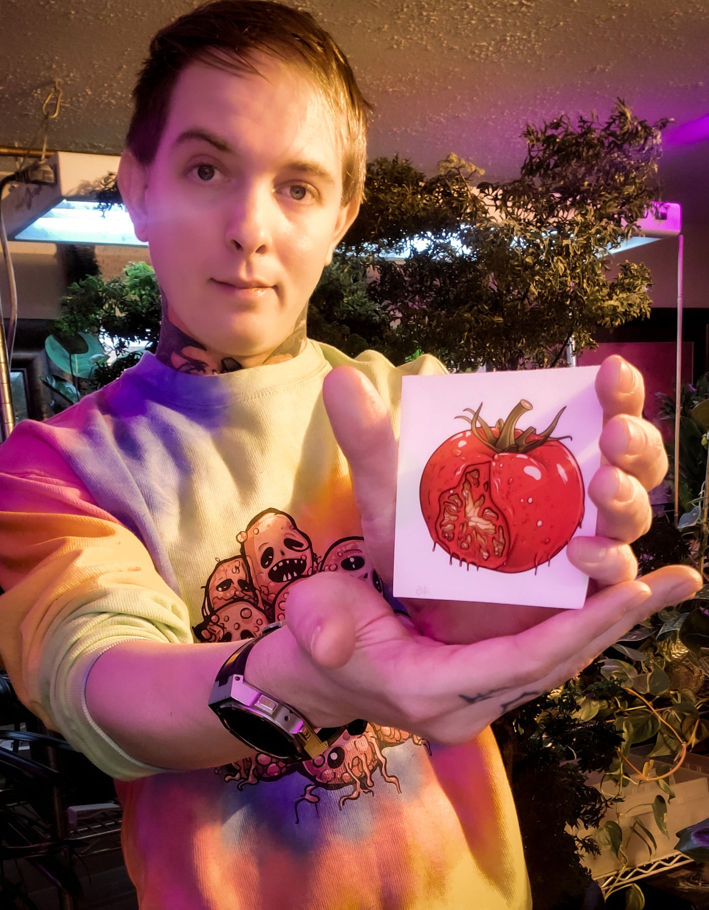 Smiling individual presenting a creepy tomato sticker, vibrant indoor garden backdrop.