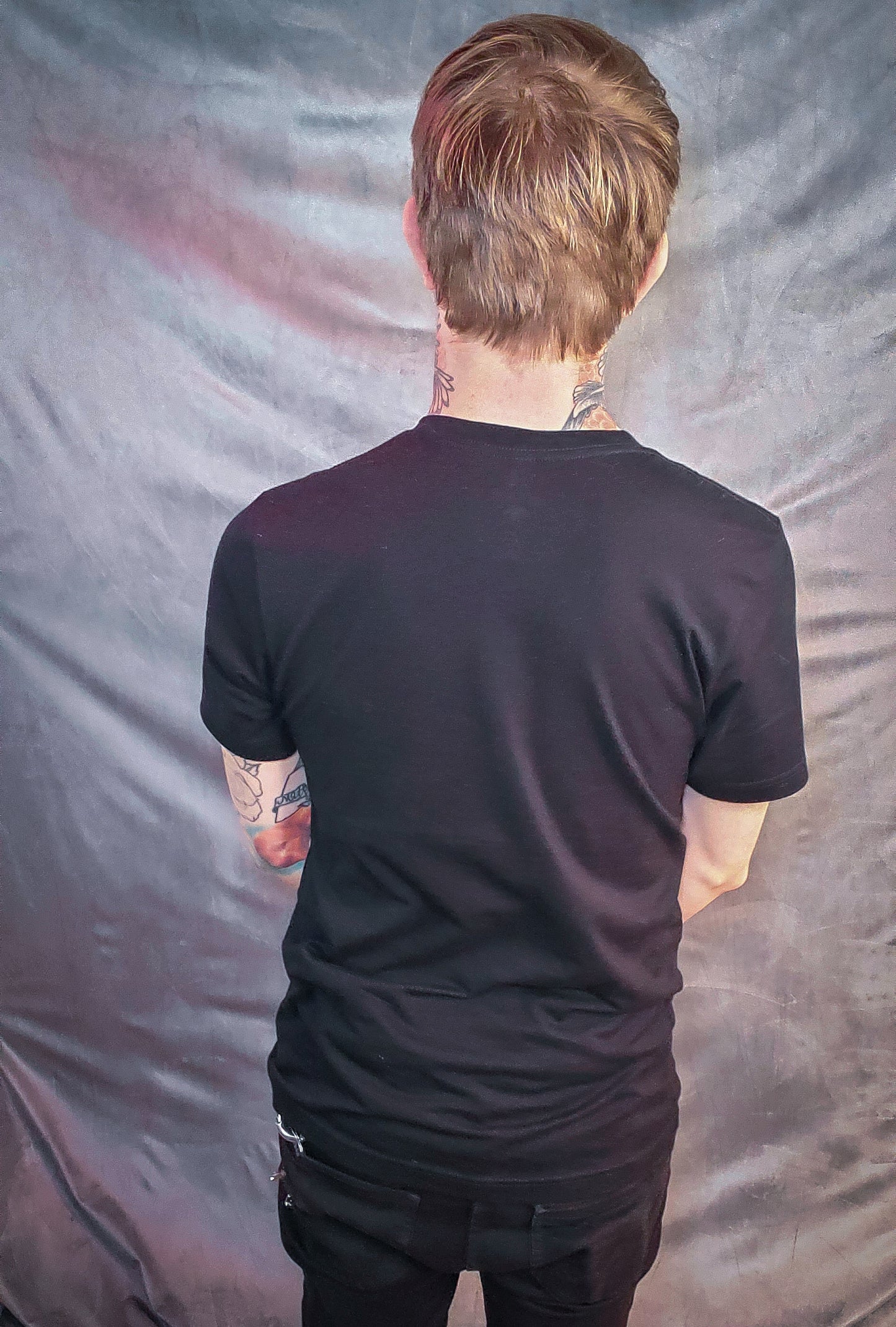 Rear view of a tattooed individual wearing a sleek black t-shirt