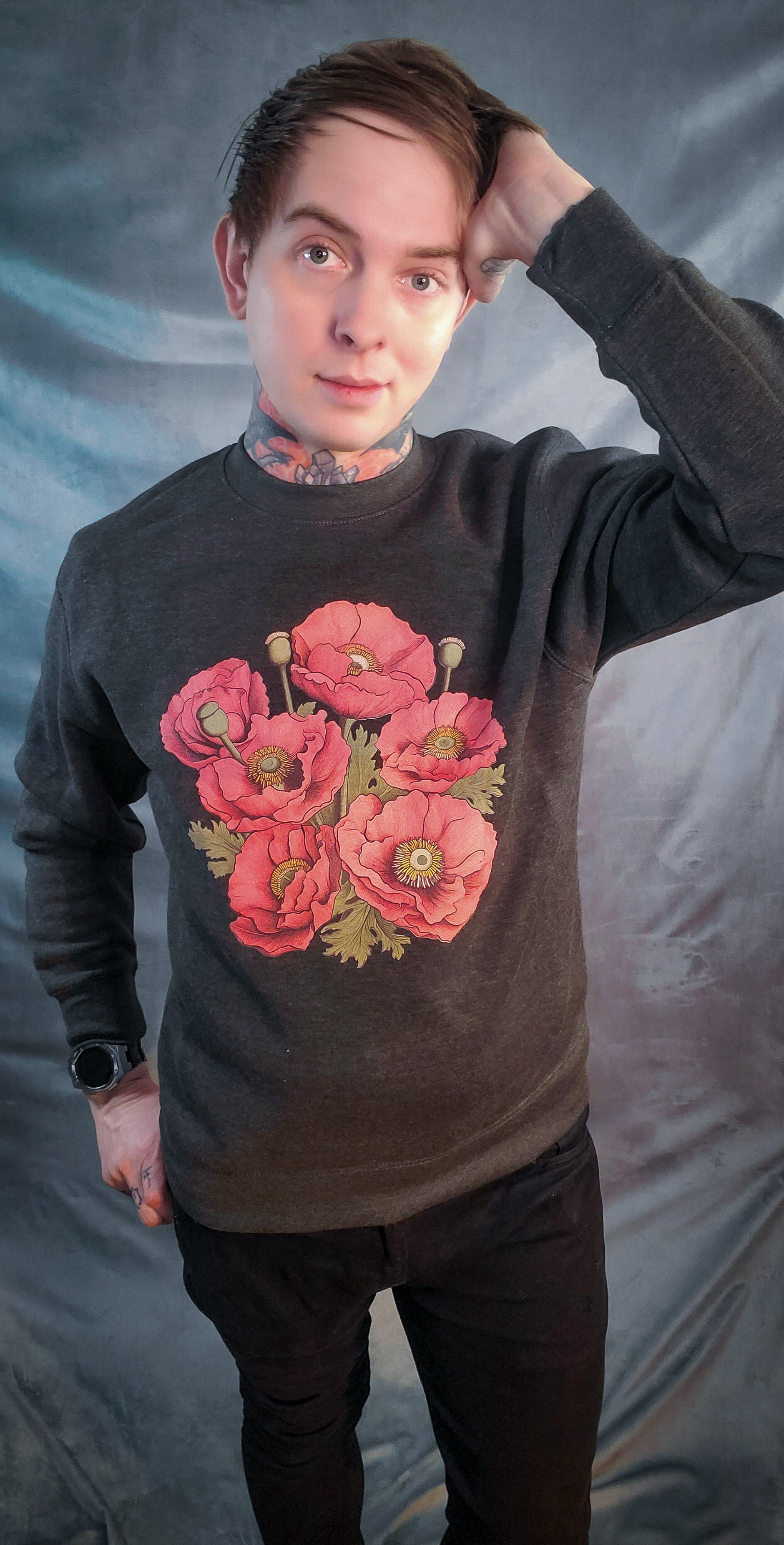 Individual in a dark sweatshirt with vibrant red poppy print resembling eyeballs, standing against a grey backdrop