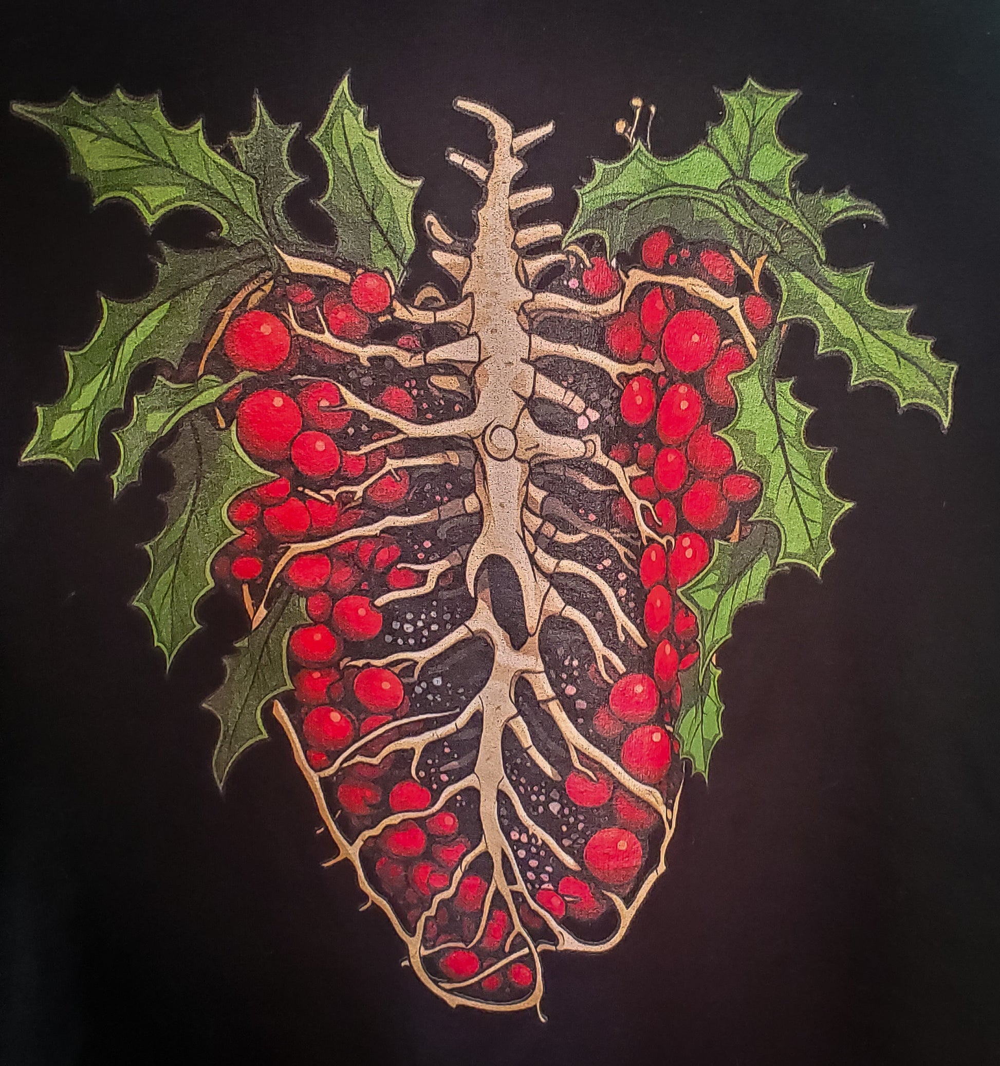 Close-up of dark T-shirt graphic with holly-adorned ribcage design, combining festive elements with gothic style.