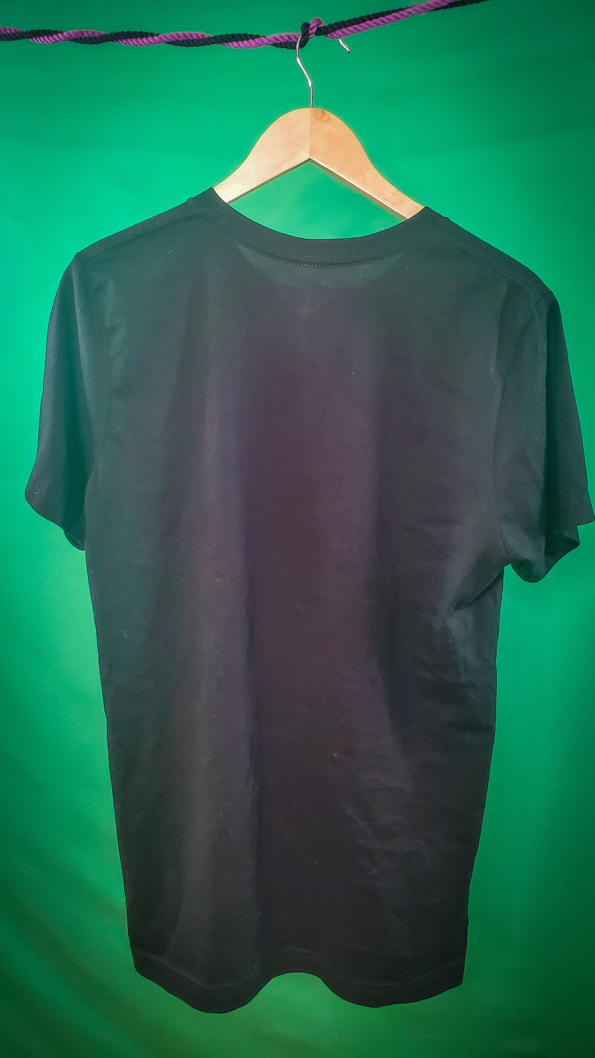 Rear view of a black T-shirt on a wooden hanger against a bright green background