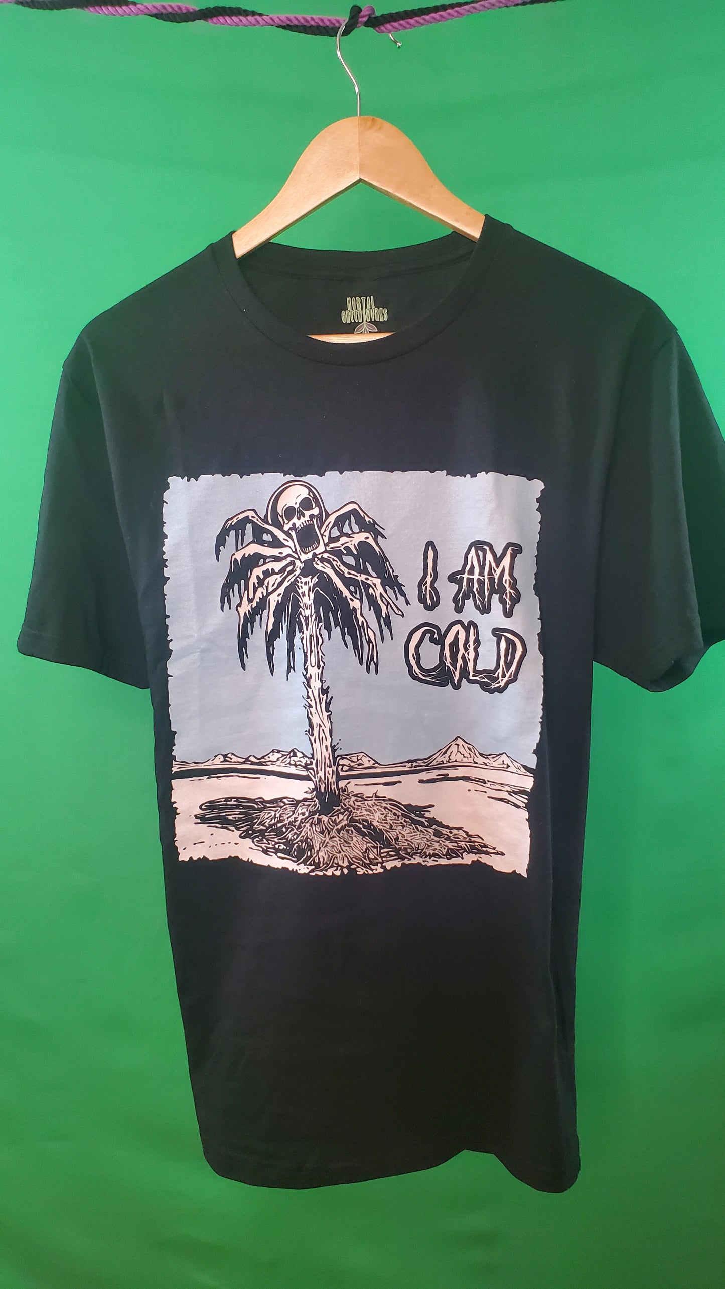 Black T-shirt with a chilling design of a frozen palm tree in a desolate desert and a skull screaming from its top, captioned 'I AM COLD.