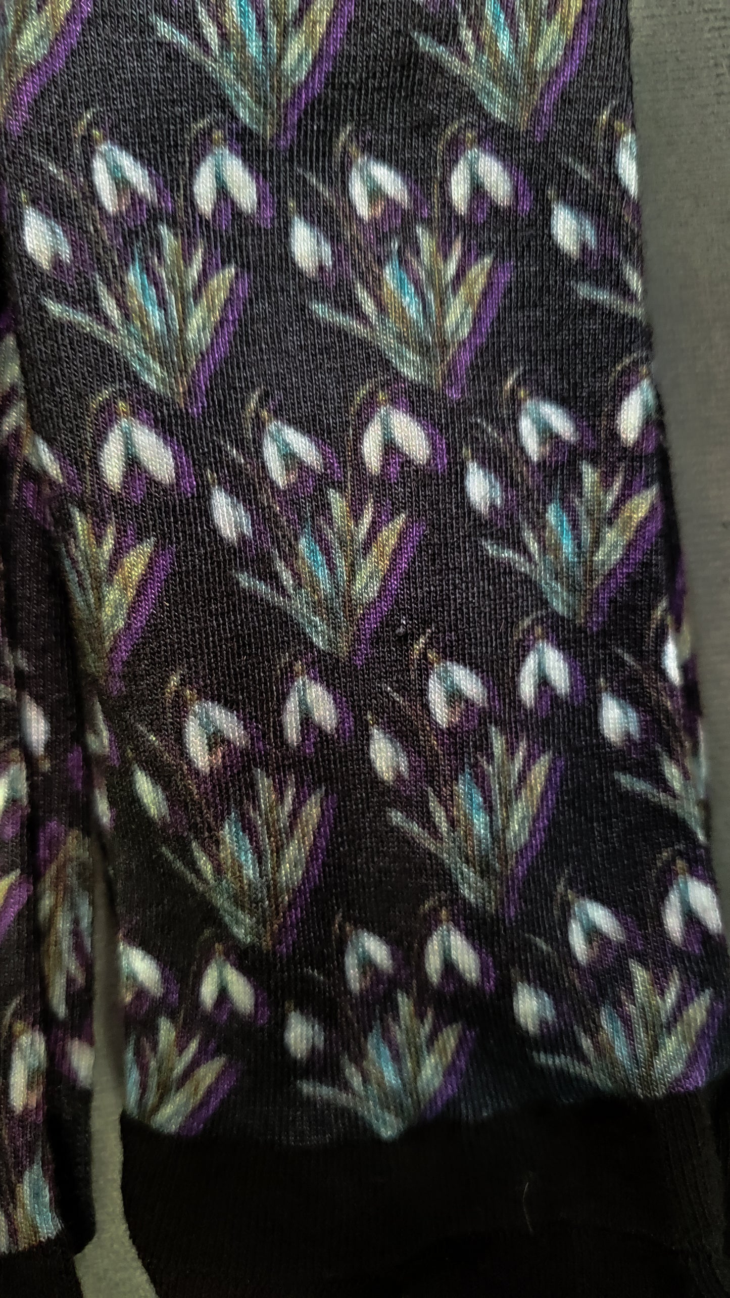 Close-up of charming socks adorned with a colorful snowdrops pattern, offering a botanical twist to everyday wear against a backdrop of indoor greenery.