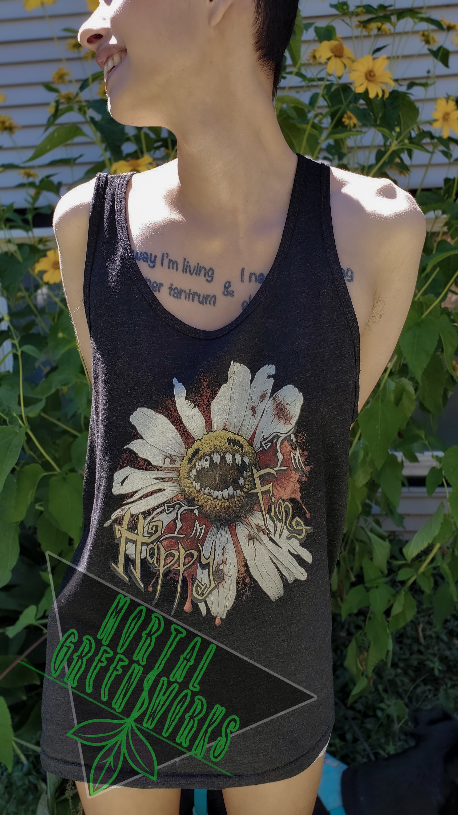 Close-up of a person smiling and looking away while wearing a black tank top with a "Diseased Daisy" graphic and the text "I'm Happy I'm Fine." Yellow flowers are in the background. The Mortal Greenworks logo overlays the image.