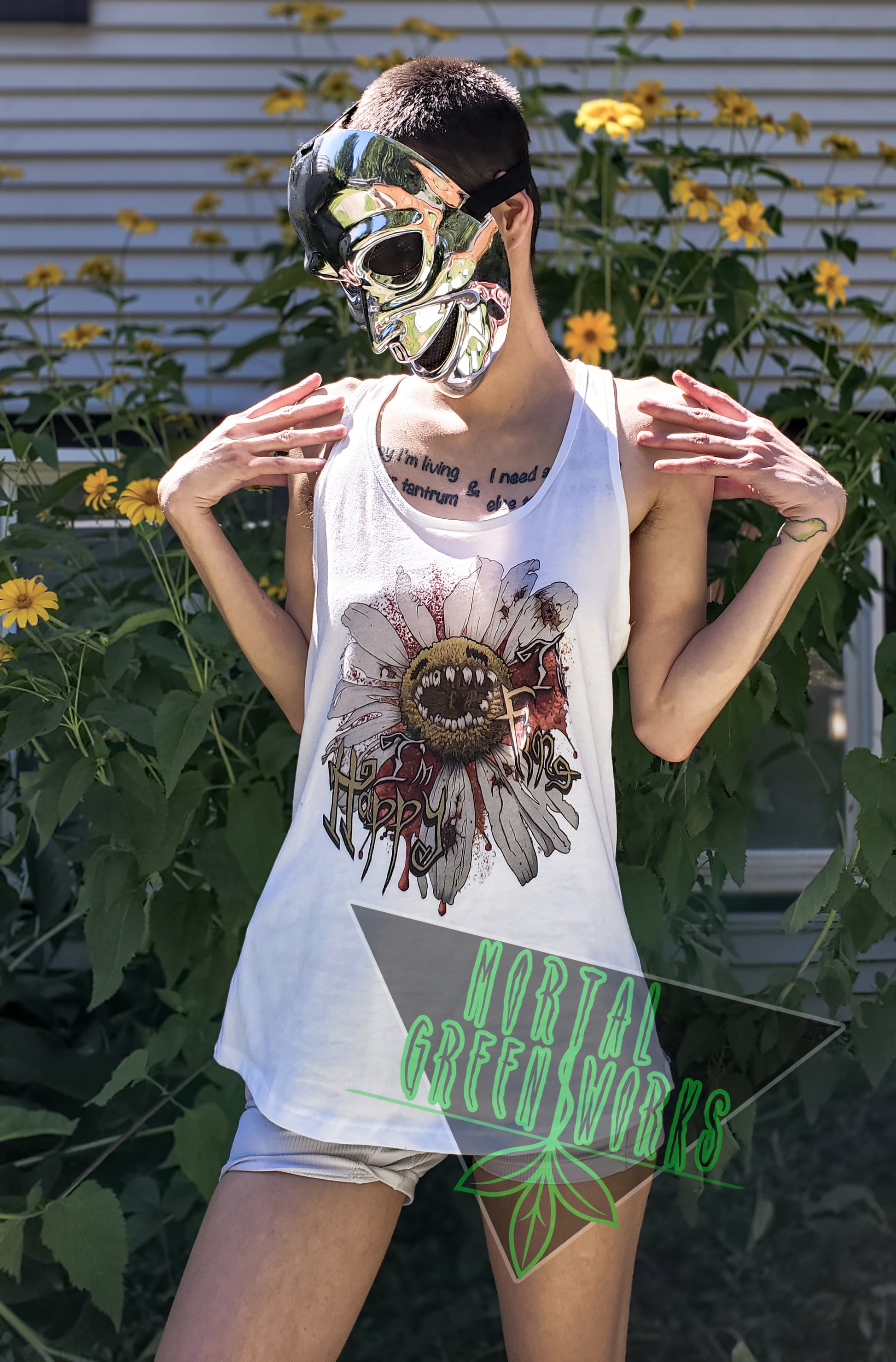 Person wearing a chrome mask and a white tank top with a "Diseased Daisy" graphic and the text "I'm Happy I'm Fine." They stand in front of yellow flowers. Mortal Greenworks logo overlays the image.