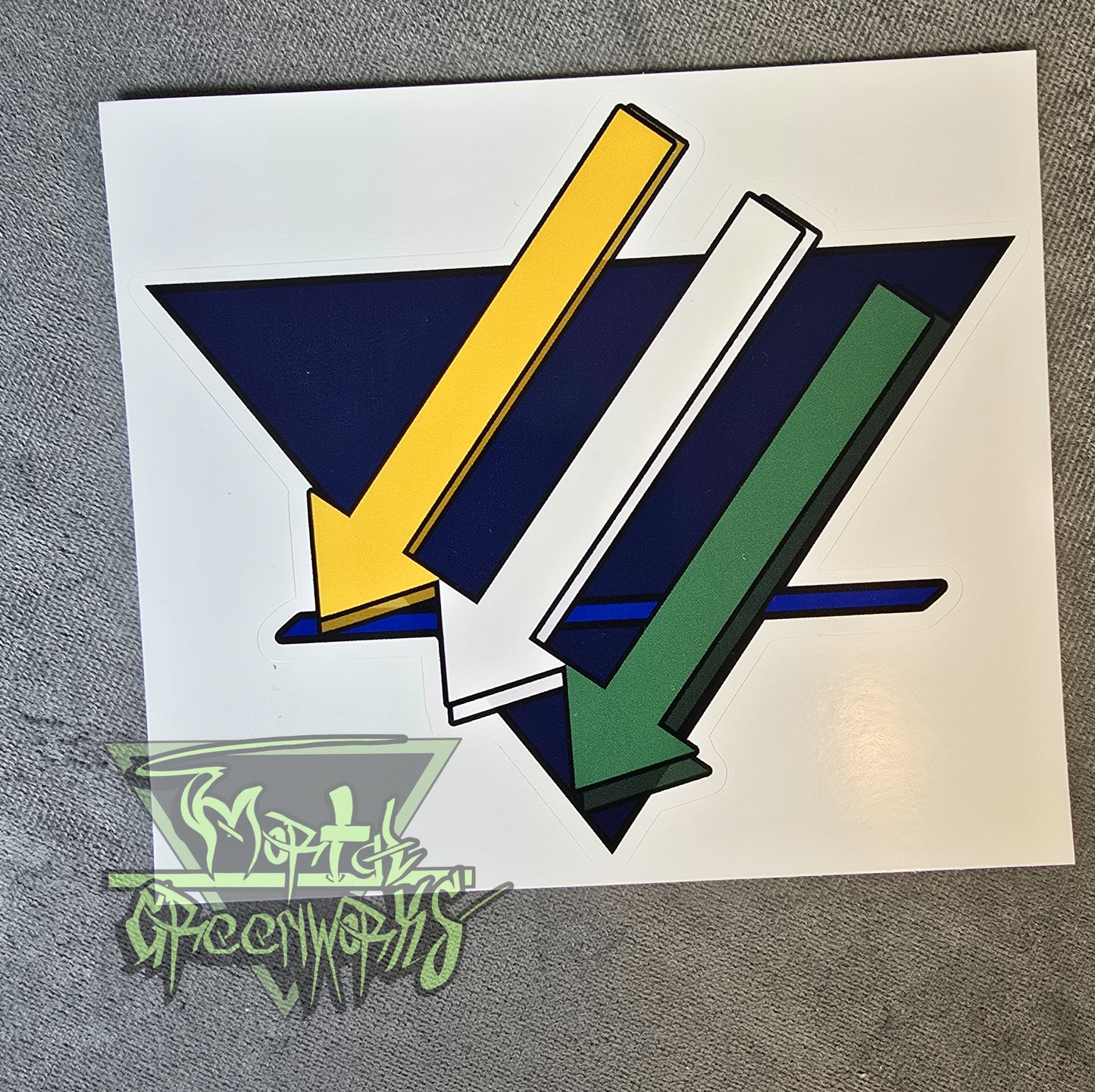 Close up of a 6x6" sticker showing the three iron cross down arrows painted gold, white, and green, are on a dark blue upside down triangle with a lighter blue bold line in the bottom third T.he Mortal Greenworks Logo sits in the bottom left corner