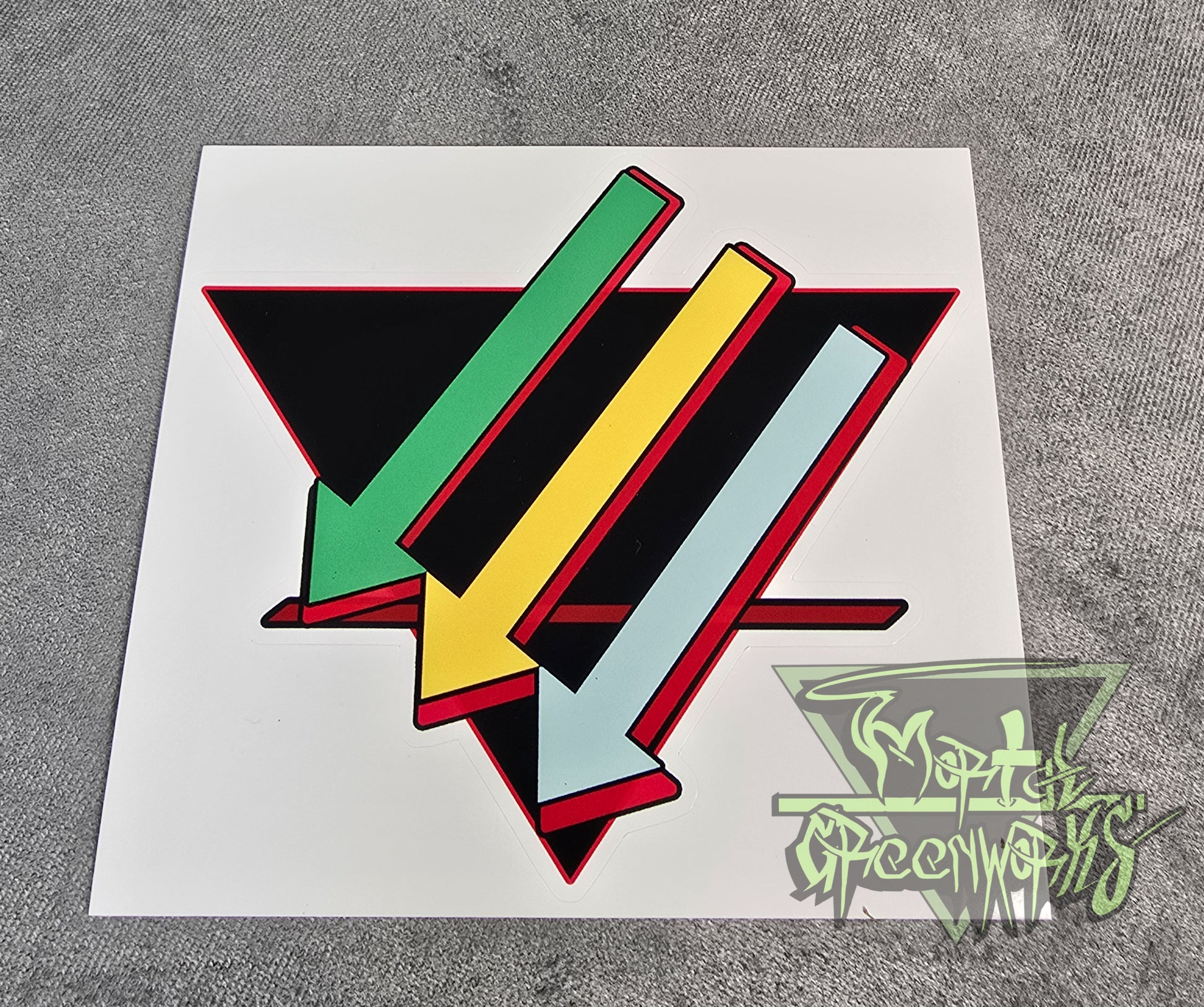 Photo of a colorful geometric design on a 6x6 sticker sheet with a brand logo in the corner of the photo. Three arrows, top to bottom: light green, gold, and turquoise, are paired against a black upside-down triangle and a red line in the bottom third. 