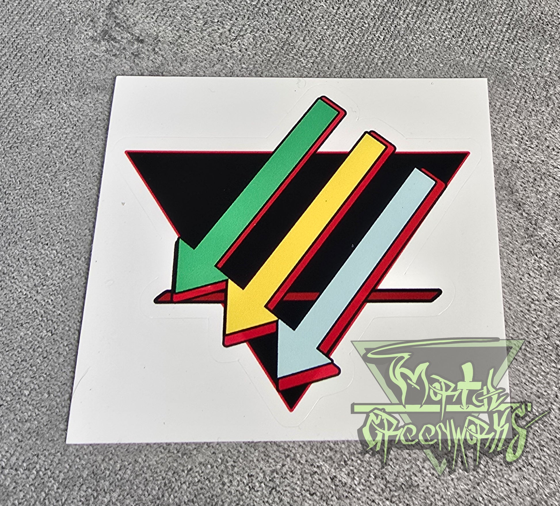 Photo of a colorful geometric design on a 4x4 sticker sheet with a brand logo in the corner of the photo. Three arrows, top to bottom: light green, gold, and turquoise, are paired against a black upside-down triangle and a red line in the bottom third. 