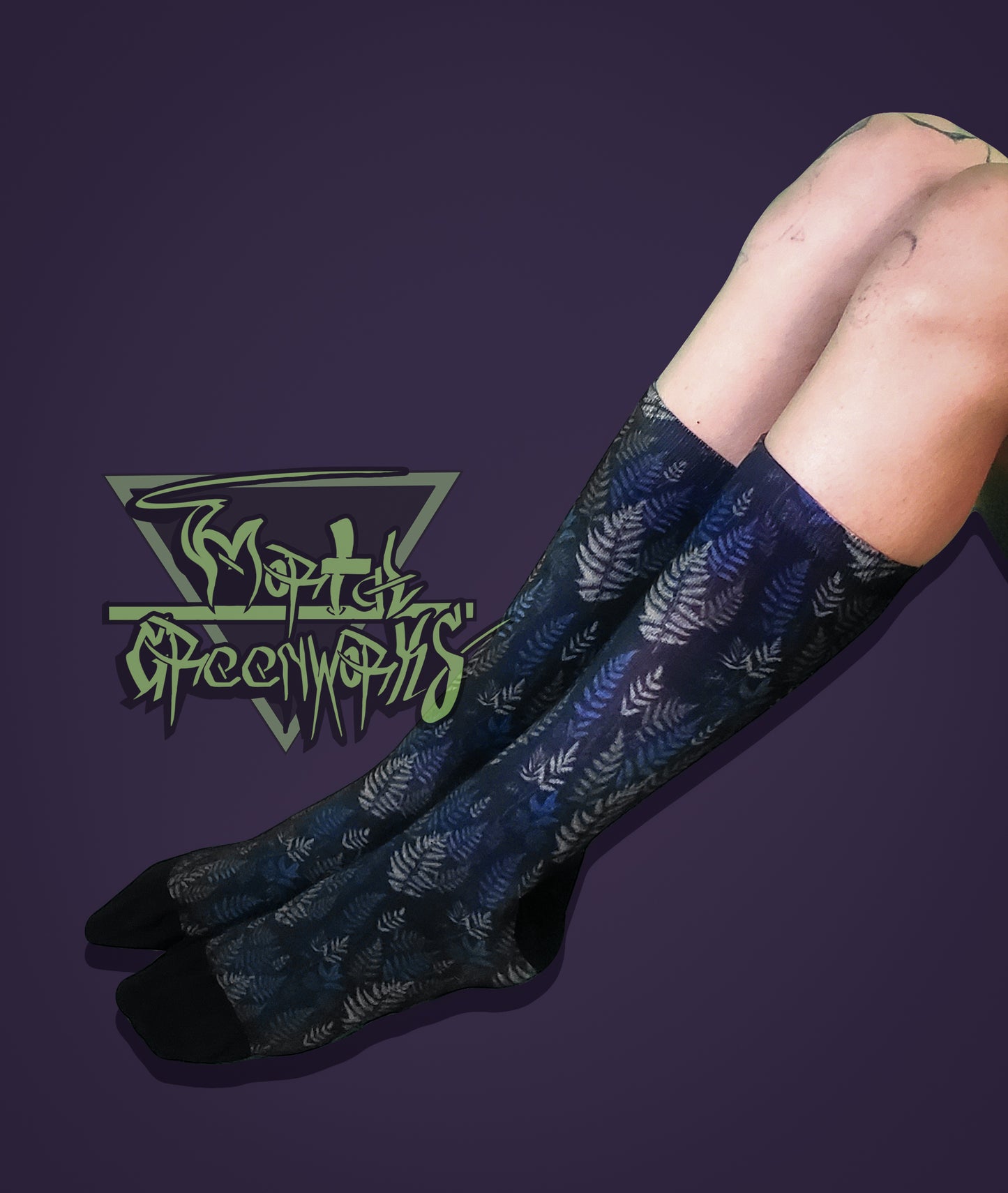 Person wearing black socks with a green and purple fern fronds pattern on a purple background, featuring a logo in the corner.