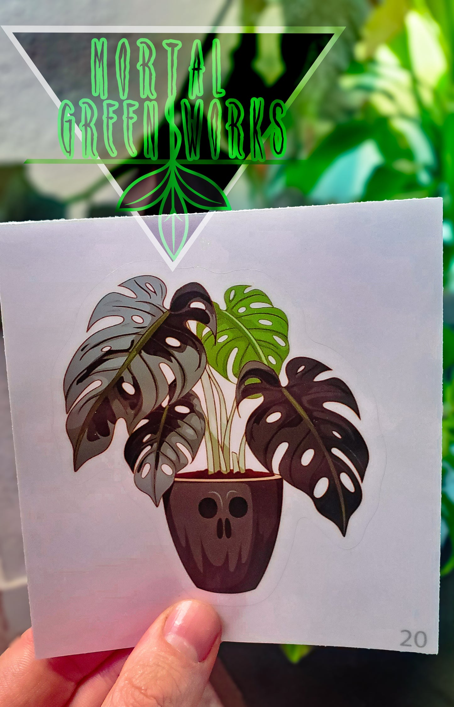 A sticker of a skull-faced pot with a monstera plant held against a green background with the 'Mortal Greenworks' logo above.