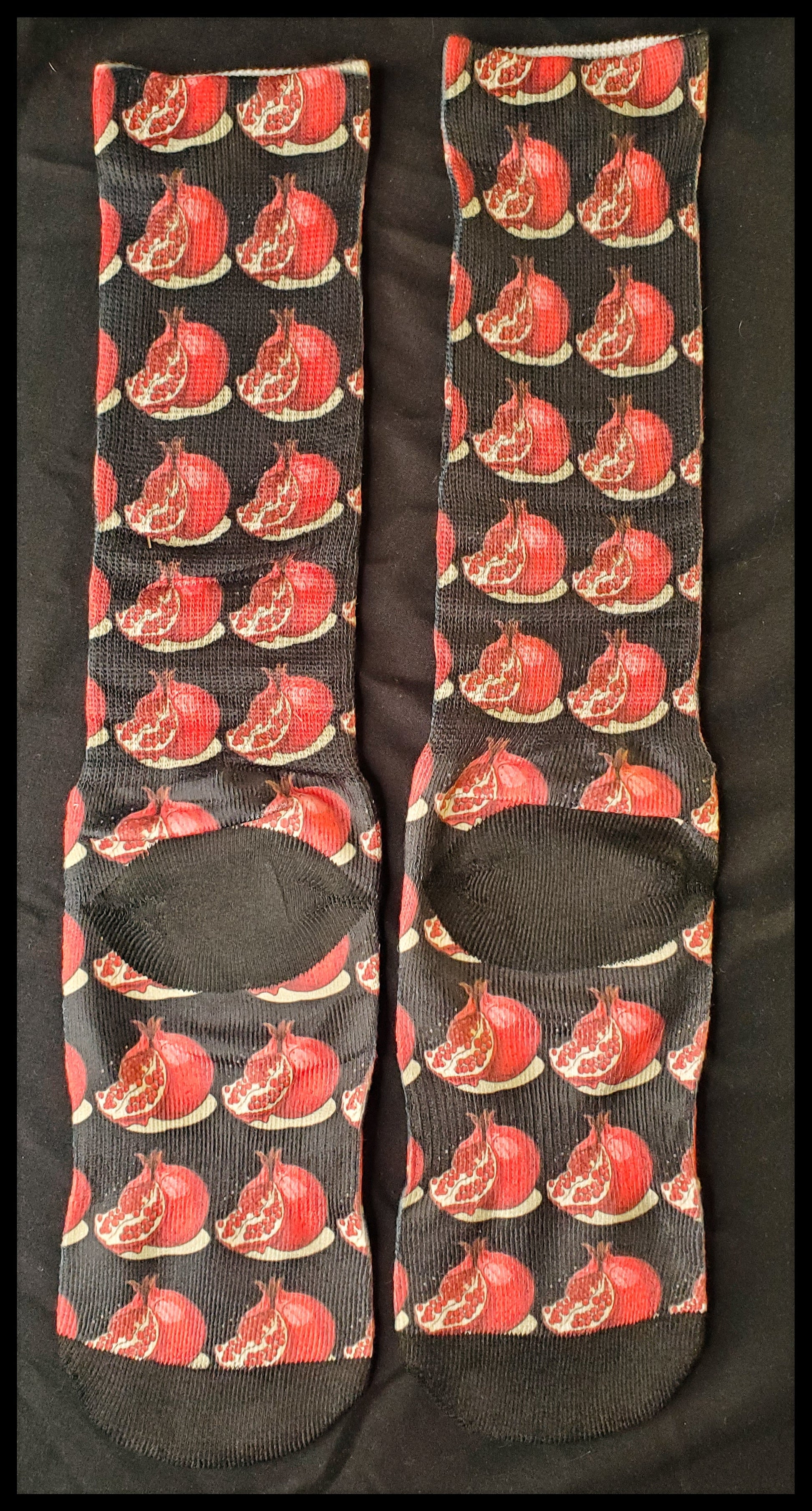 The socks display a repeated pattern of red pomegranates with exposed seeds on a dark background, creating a striking visual texture.
