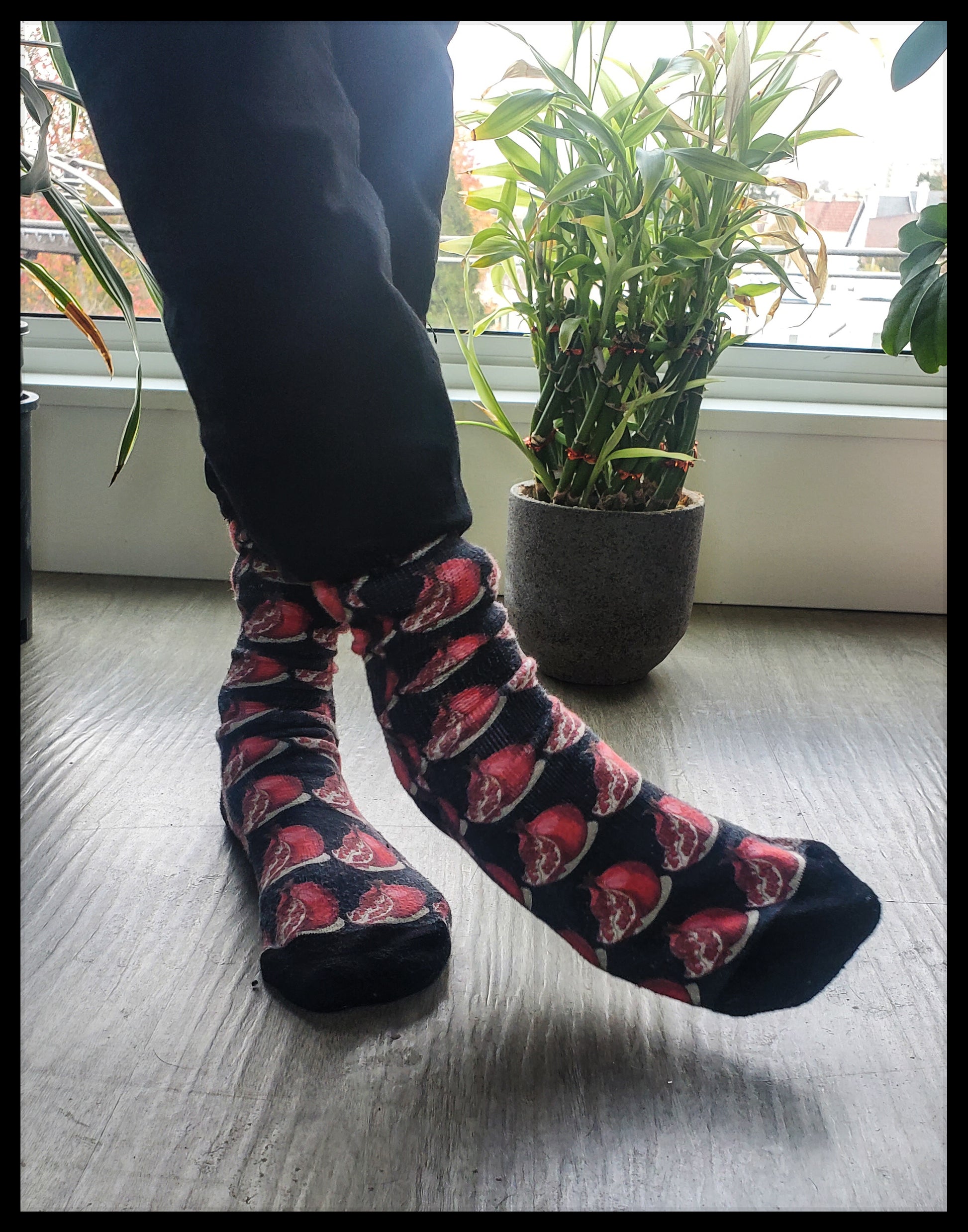 The socks feature a bold pattern of red pomegranates set against a dark backdrop, accentuating the fruit's vibrant hue and detailed design.