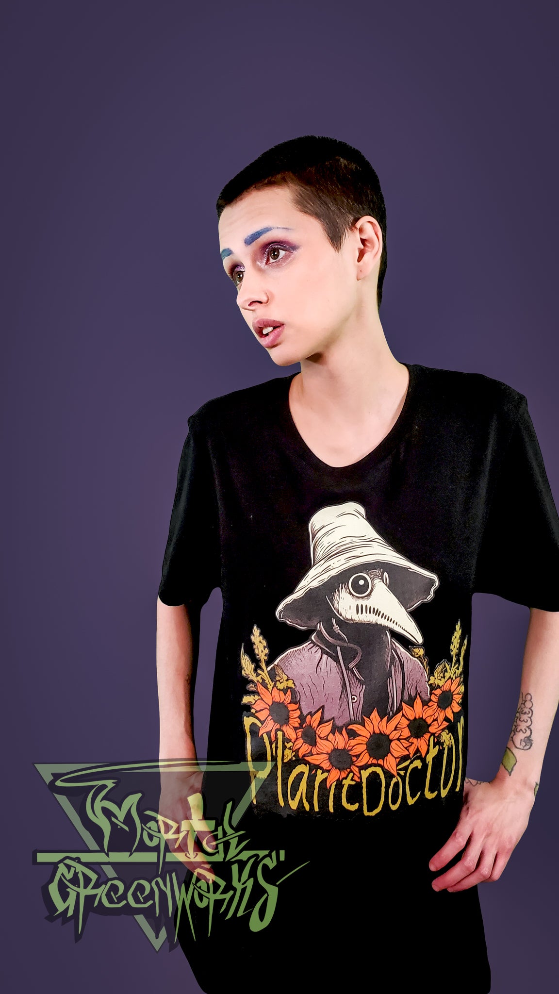 Person with tattoos wearing a black t-shirt with a graphic design that says "plant doctor" on a purple background