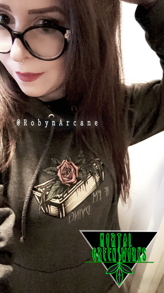 Individual posing in a black hoodie with a rose and coffin design and 'IF I'M DYING' text, under the Mortal Greenworks logo, tagged @RobynArcane.