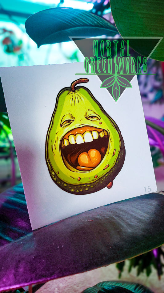 A sticker with a grinning avocado character placed on a rubber tree leaf, with 'Mortal Greenworks' branding in view.