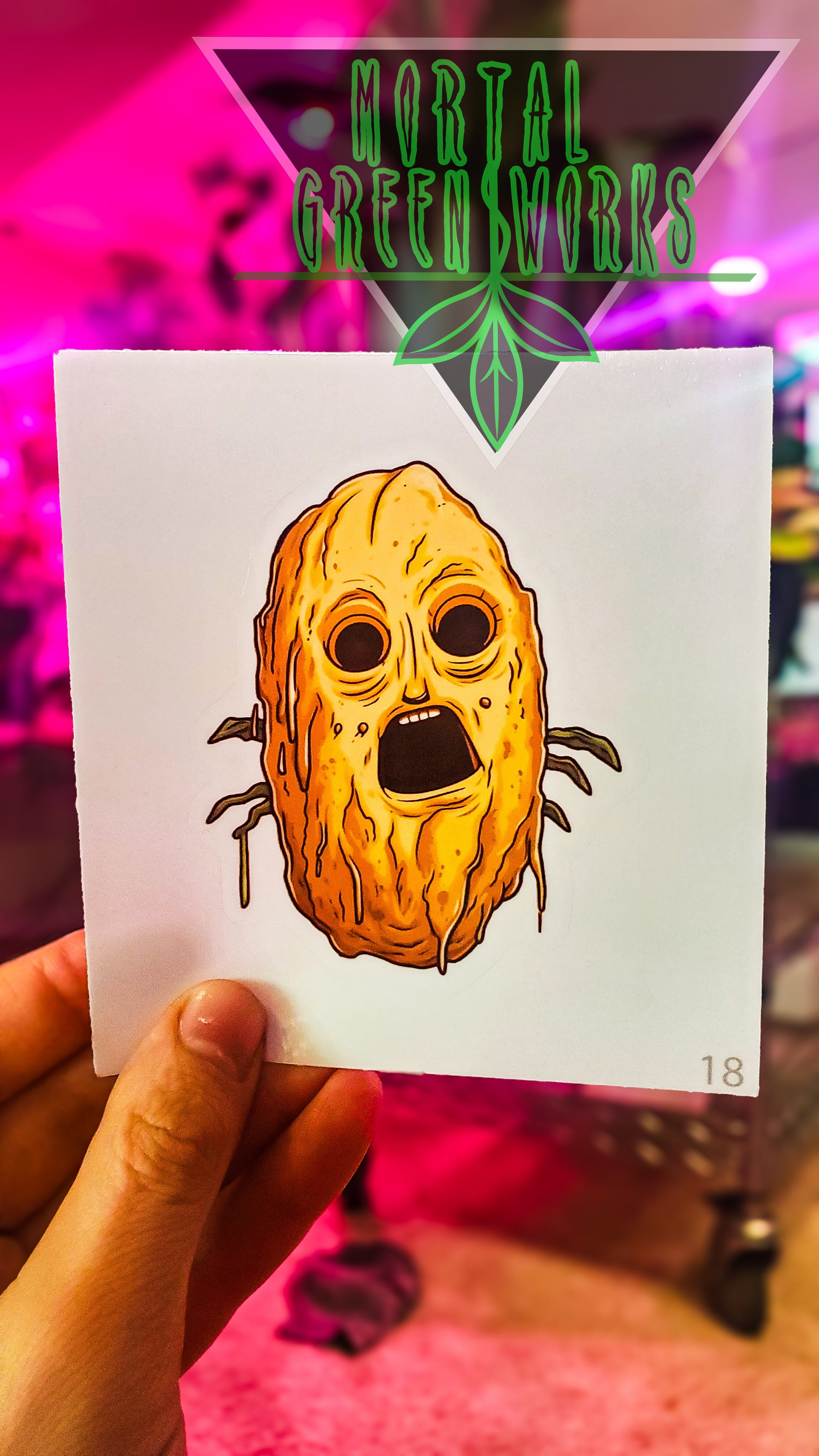 A hand holds a sticker depicting a horrified potato with a face, set against a colorful blurred background, with 'Mortal Greenworks' branding above.