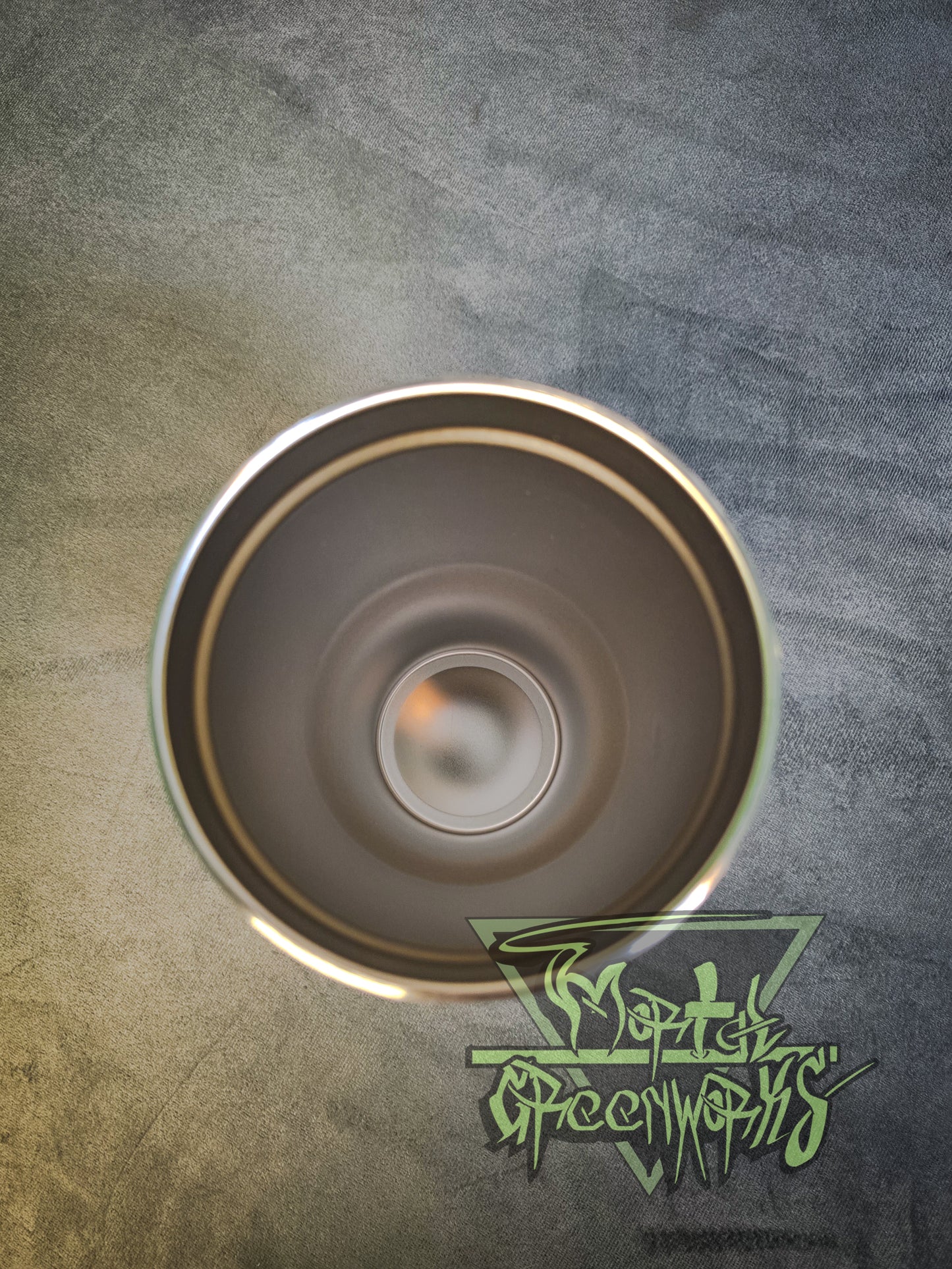 A bird 's-eye view of the inside of the 30-oz tumbler, clean and shiny. The Mortal Greenworks logo lingers in the bottom right hand corner with a grey table cloth in the background.