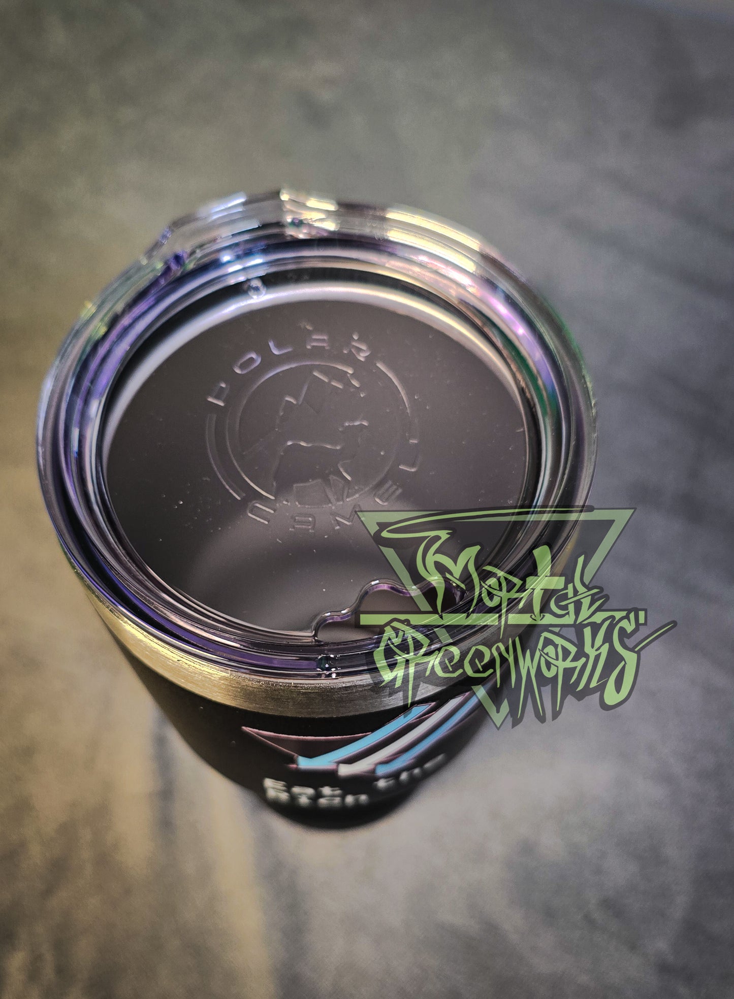 A close up image of a black tumbler cup with the climate front trans pride logo creeping around the cup, barely visible. You can see the inside of the steel cup, clean chrome and enclosed by a plastic lid with a mouthpiece that says Polar Camel in transparent text.
