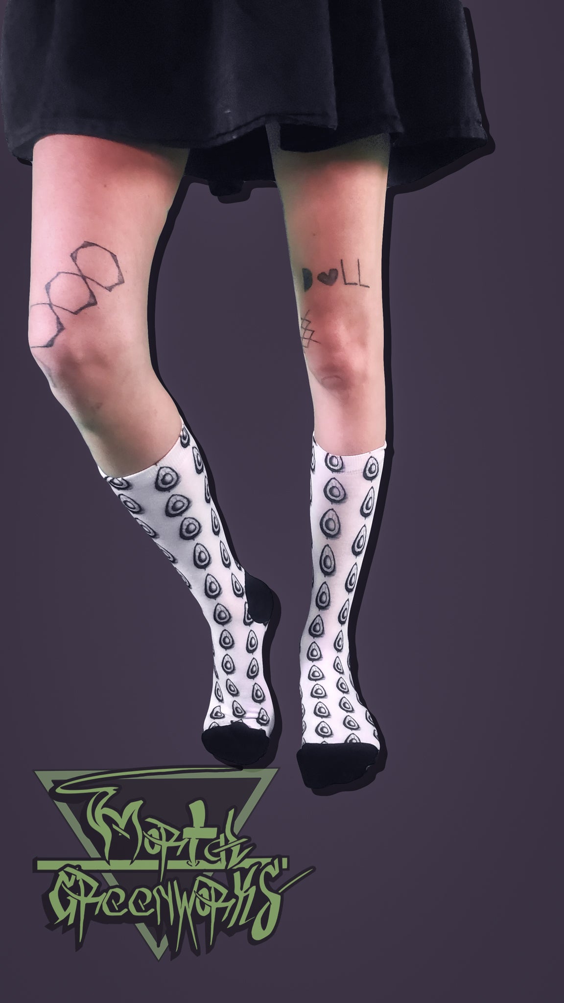 Person wearing black and white patterned avocado socks with a dark background and brand logo.