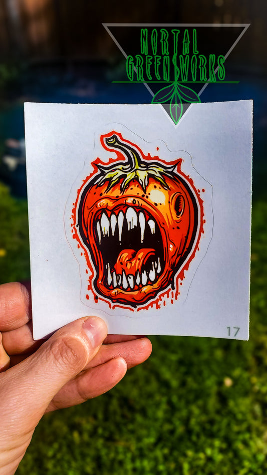 A sticker of a ferocious strawberry with sharp teeth, held in a hand, with 'Mortal Greenworks' logo above.