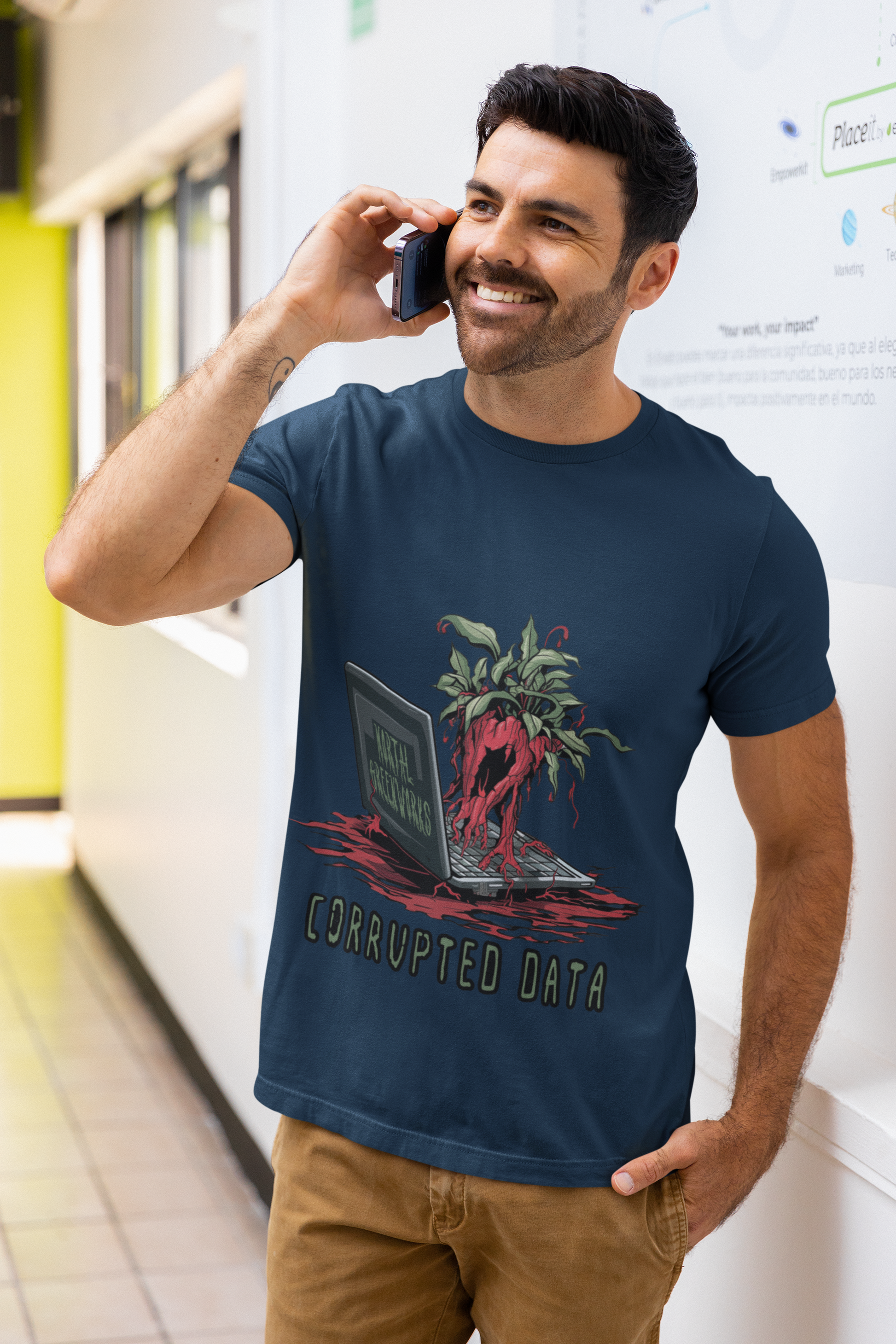 Man in a navy t-shirt featuring a "corrupted data" design with a bleeding plant emerging from a laptop, paired with brown pants.