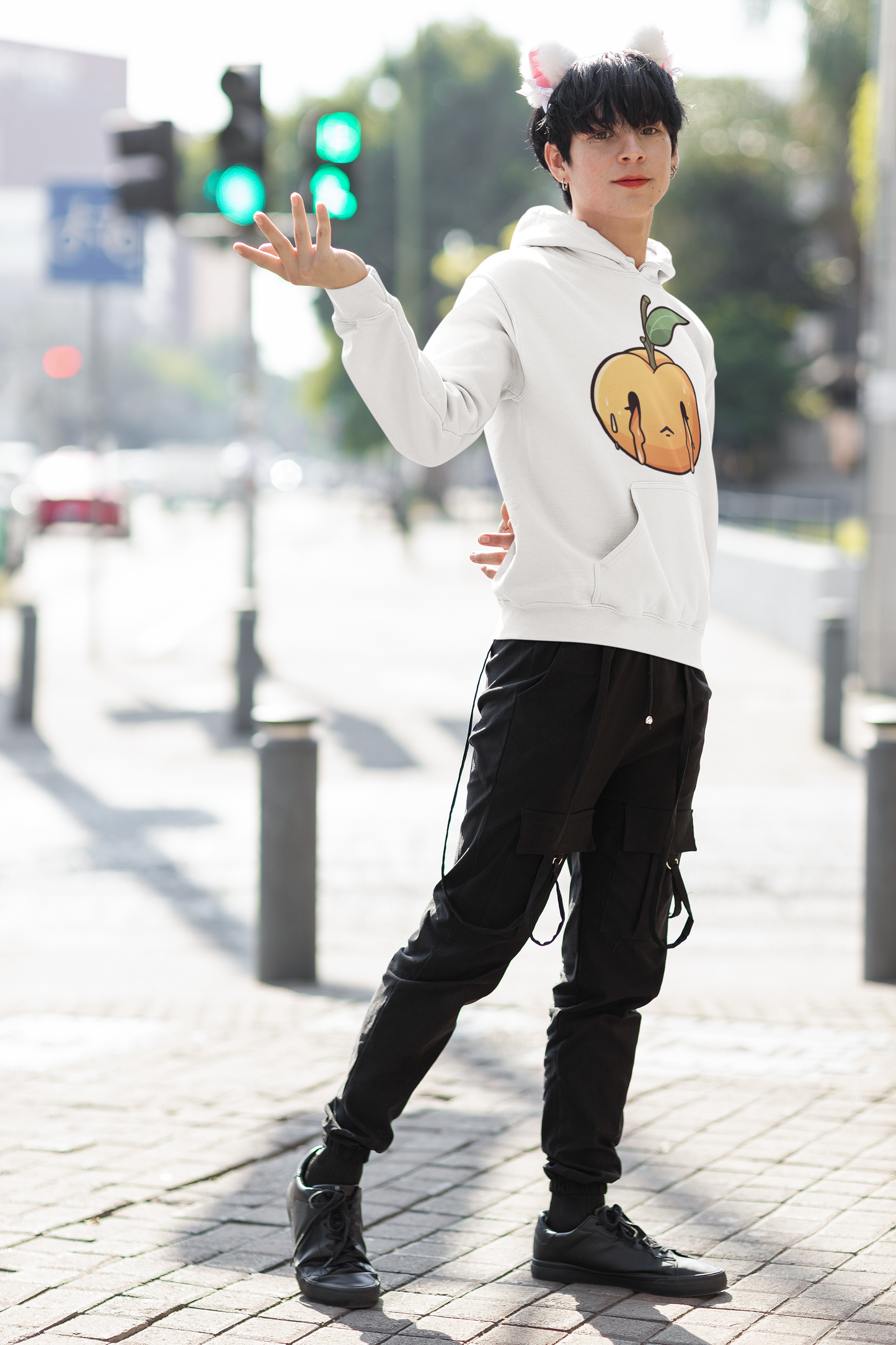 Person in urban setting, wearing a white hoodie with a melting peach design, striking a playful pose.