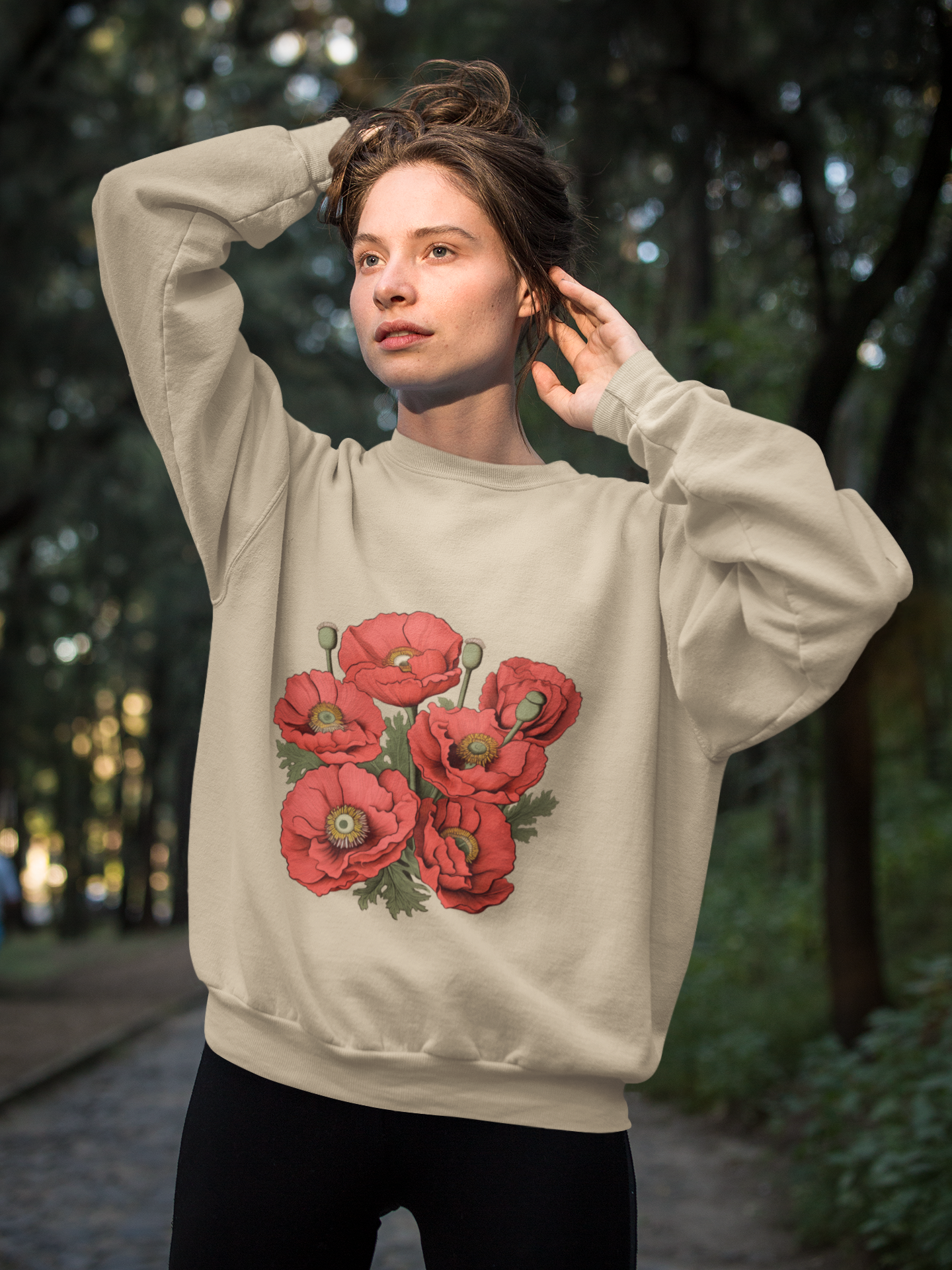 A woman outdoors in a beige sweatshirt adorned with red poppy graphics, looking upwards.