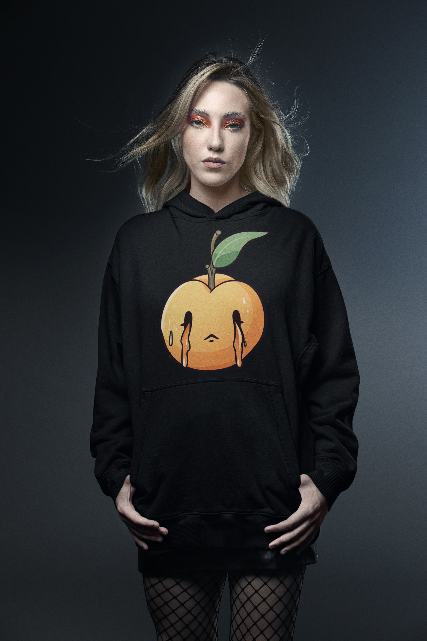 Woman with dramatic makeup, wearing a black hoodie with a melting peach graphic design, against a dark backdrop.