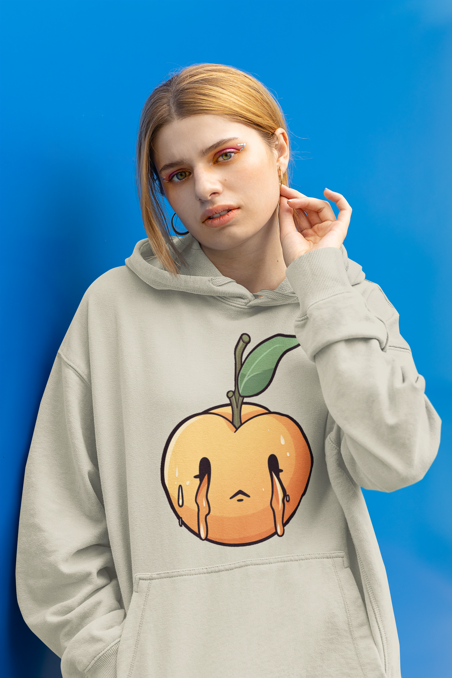 A woman is posing against a blue wall wearing a hoodie with a melting peach design on the front.