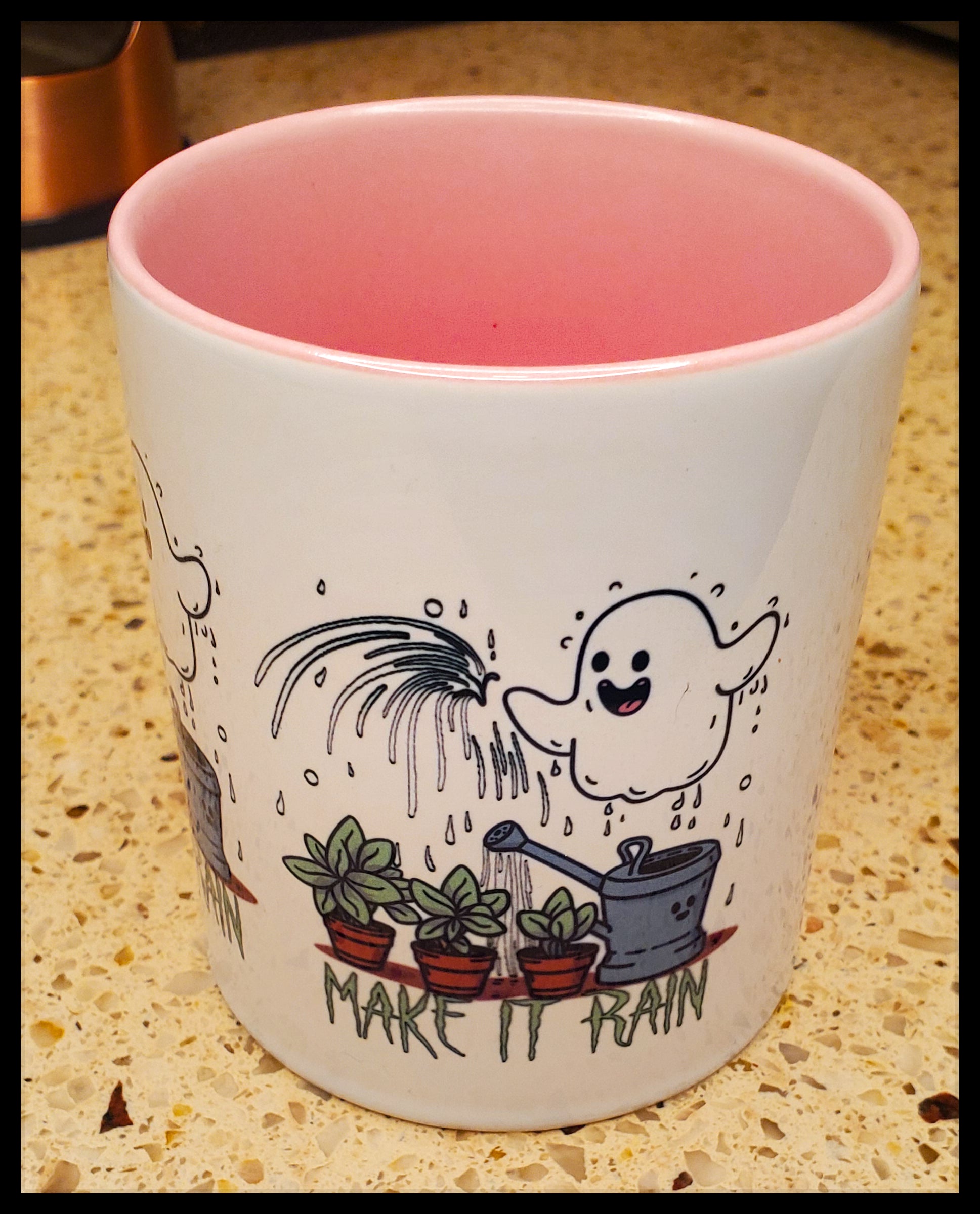 The mug has a playful design with a cheerful ghost pouring water over potted plants, accompanied by the phrase "Make it rain." The inner color of the mug is pink, complementing the light-hearted and whimsical illustration.